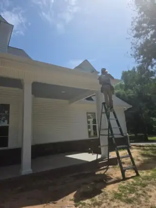 Technician on ladder installing seamless gutters on white home addition in White Hall, Arkansas