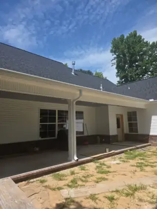 New white home with dark roof and installed gutters along the front porch in White Hall, Arkansas