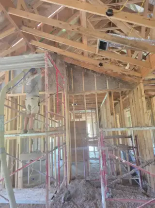 Interior of new construction home showing blown-in insulation installed in wall cavities with wooden framing and red bracing visible in White Hall, Arkansas.