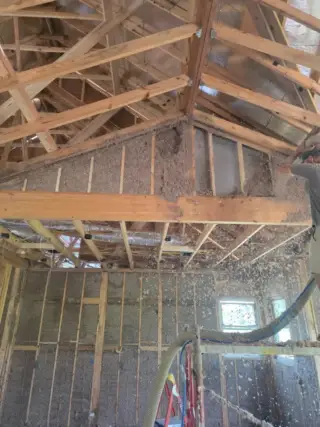 Blown-in insulation fills wall cavities between wooden framing studs during new home construction in White Hall, Arkansas.